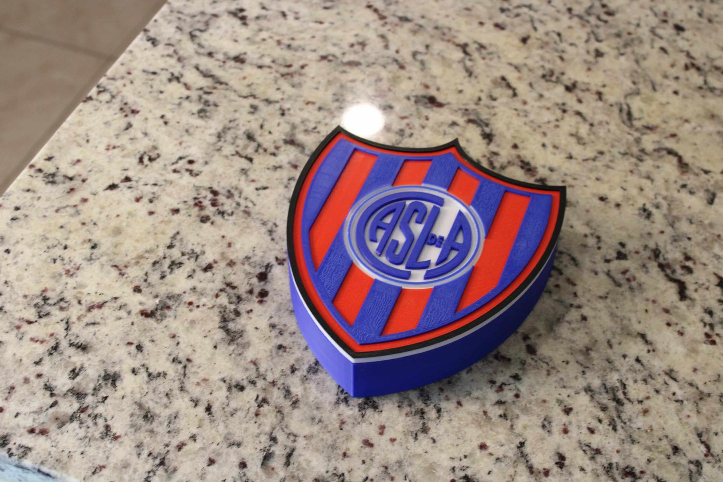 San Lorenzo 3D printed emblem on granite surface, vibrant colors, unique collectible for soccer fans.