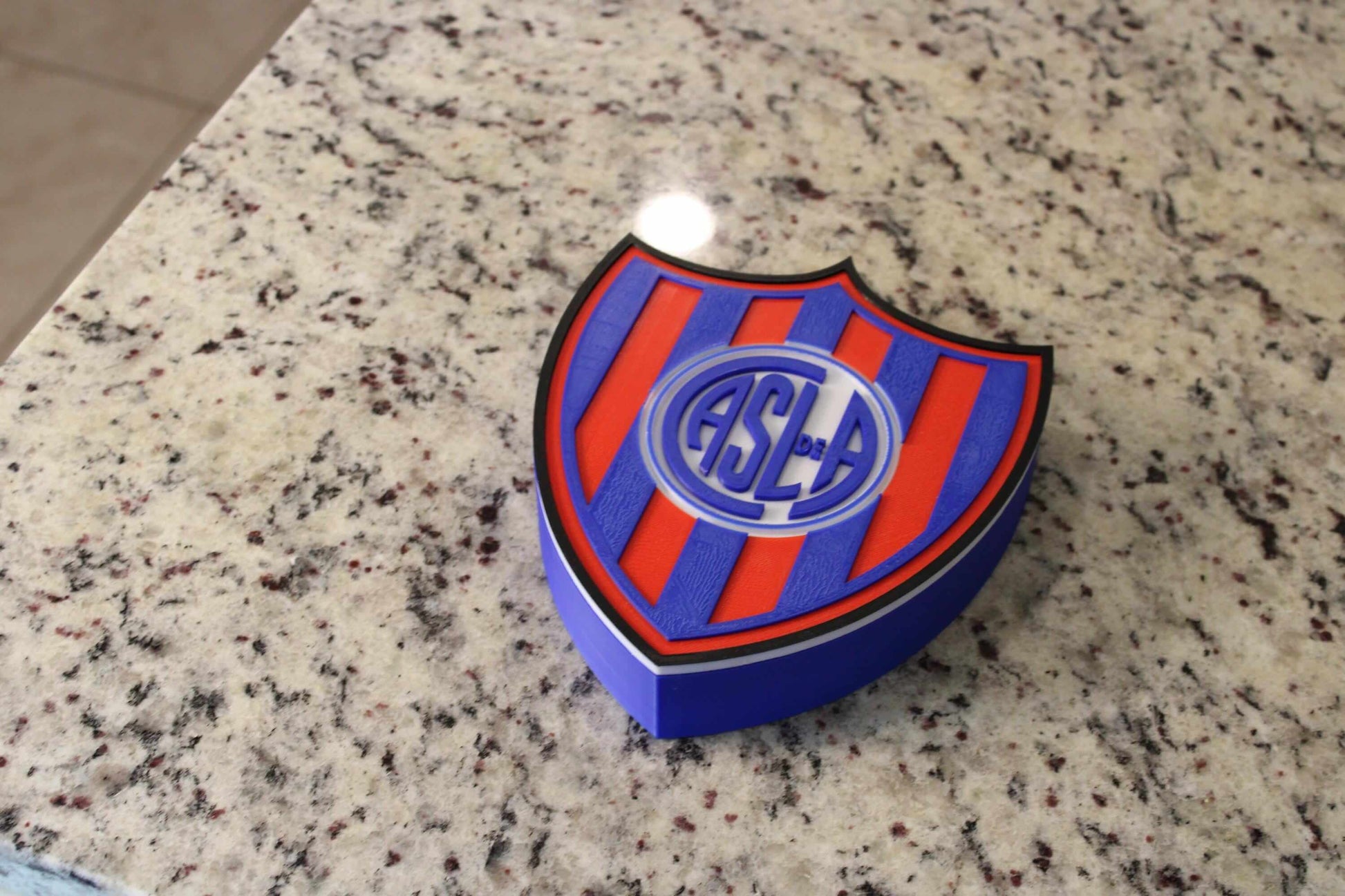 San Lorenzo 3D printed emblem on granite surface, vibrant colors, unique collectible for soccer fans.