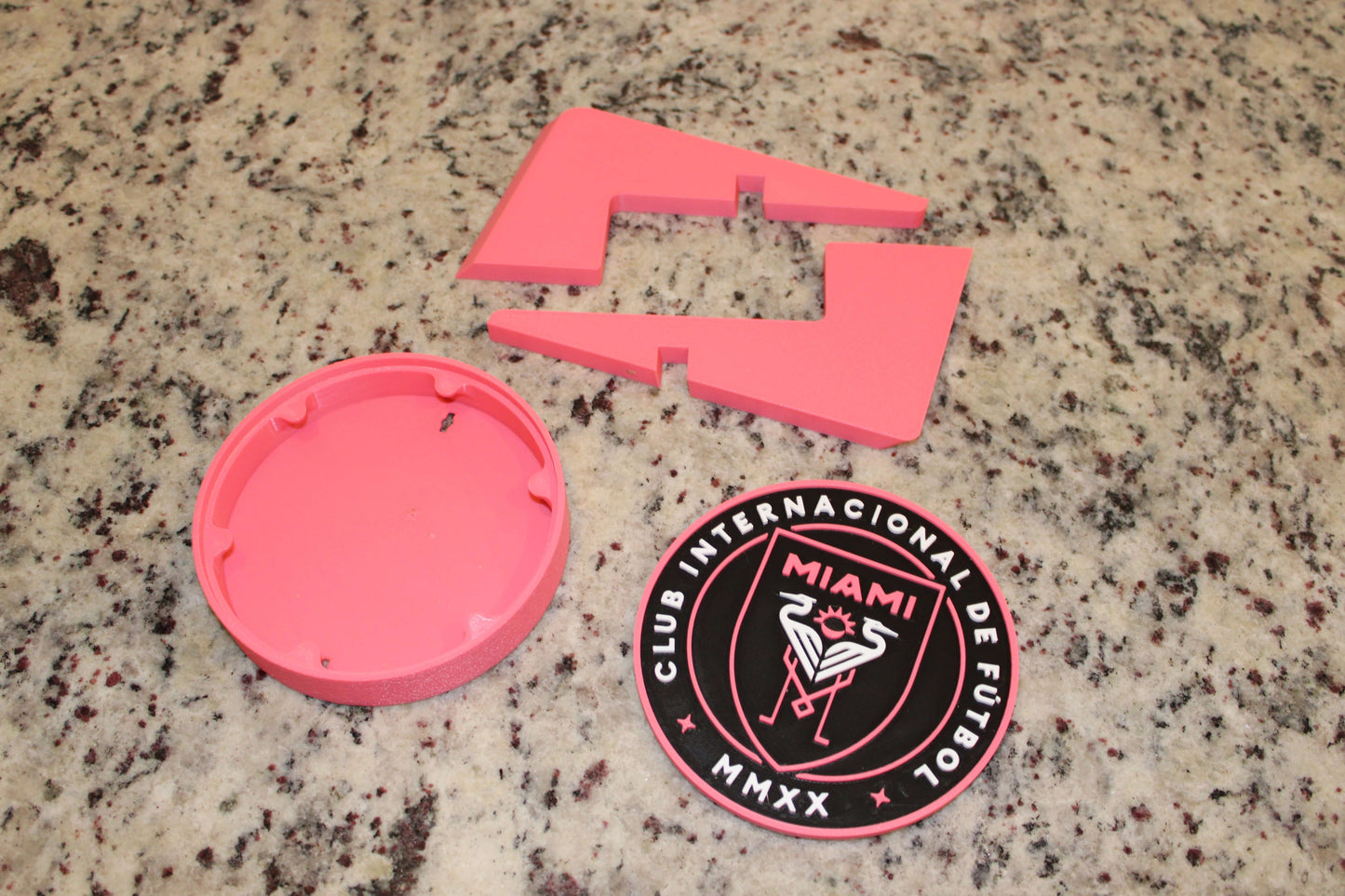 Inter Miami 3D printed emblem pieces in vibrant pink on granite surface, showcasing high quality and unique design.