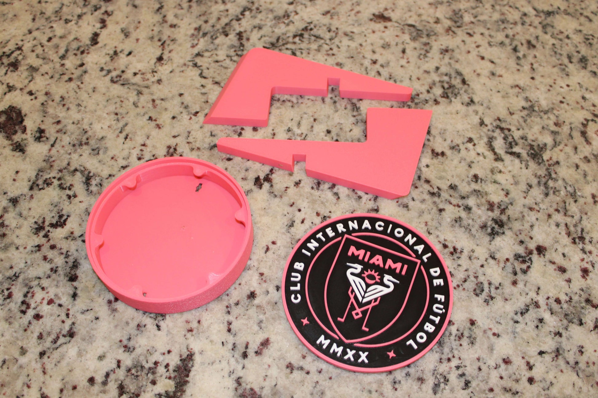 Inter Miami 3D printed emblem pieces in vibrant pink on granite surface, showcasing high quality and unique design.